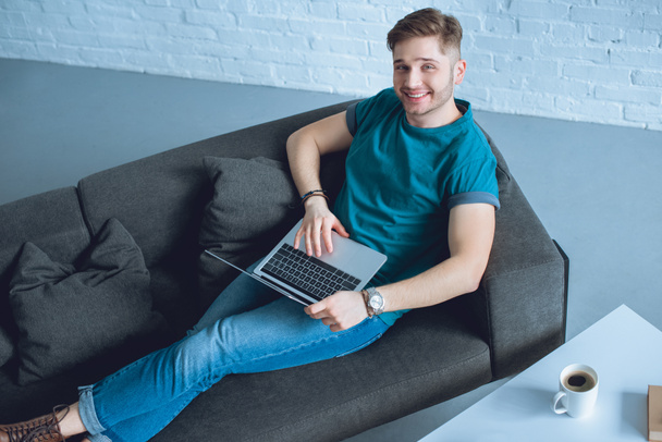 high angle view of handsome young freelancer using laptop and smiling at camera - Photo, Image