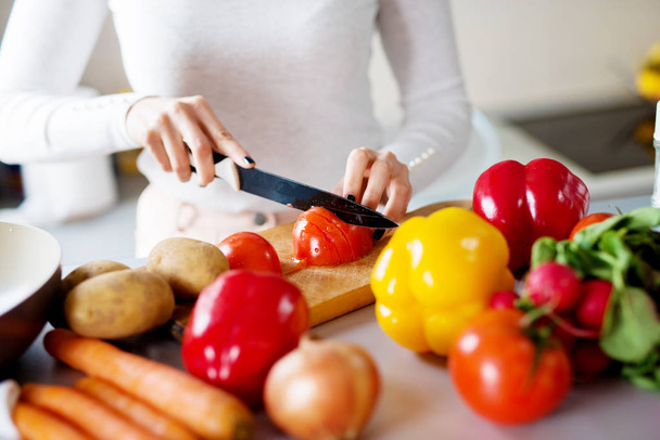 Frau schneidet Tomaten und anderes frisches Gemüse auf Küchentheke  - Foto, Bild