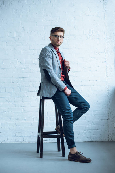 Handsome young man wearing suit sitting on tall chair - Foto, Imagem