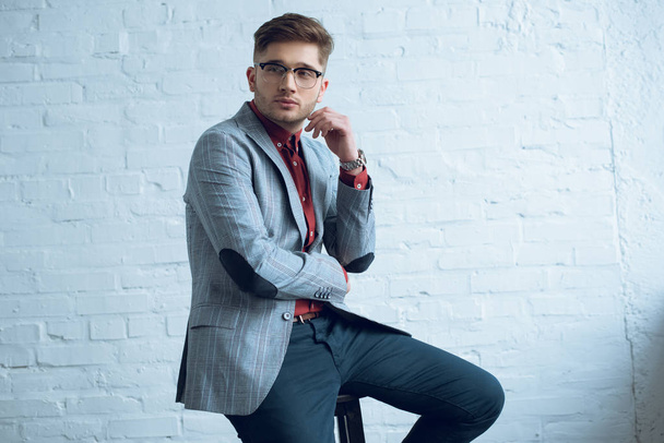 Bearded young man wearing stylish suit sitting in front of white wall - 写真・画像