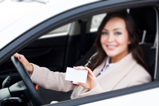 Porträt einer lächelnden Autofahrerin mit einer weißen leeren Visitenkarte. Fokus liegt auf der weißen Karte - Foto, Bild