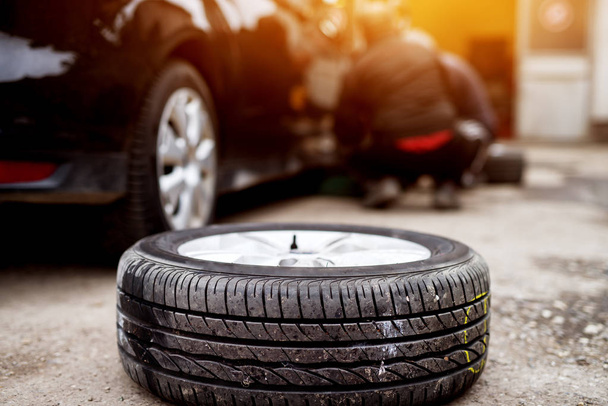 Automechaniker Mann mit Elektroschrauber wechselt Reifen in Garage, Reifen im Vordergrund - Foto, Bild