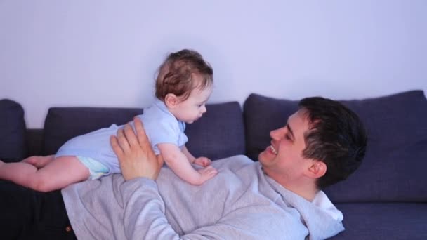 feliz padre acostado en cama sosteniendo pequeño hijo y divertirse
 - Metraje, vídeo