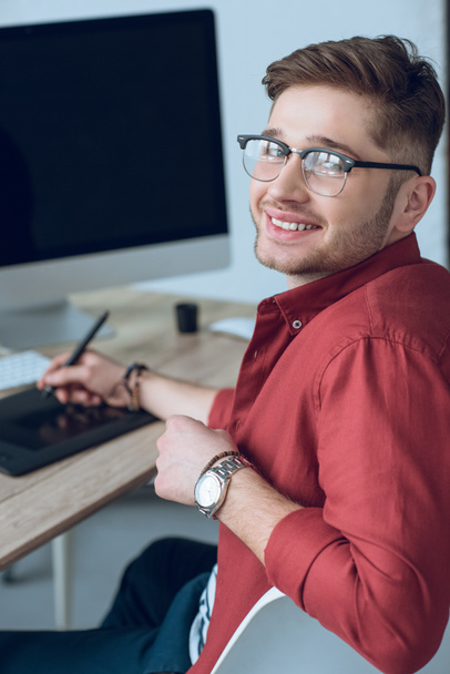 Junger lächelnder Mann am Arbeitstisch mit Grafik-Tablet und Computer - Foto, Bild