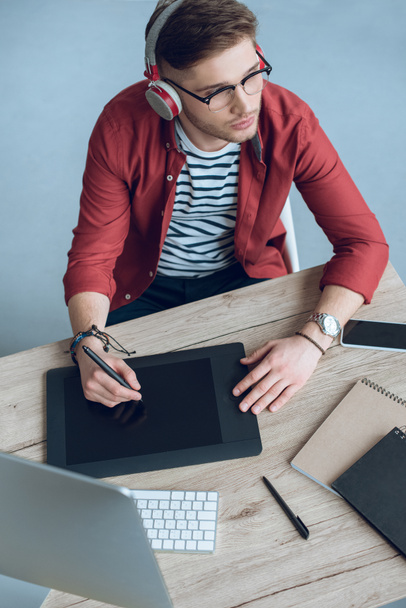 Человек-фрилансер в наушниках за работой за столом с компьютером и графическим планшетом
 - Фото, изображение