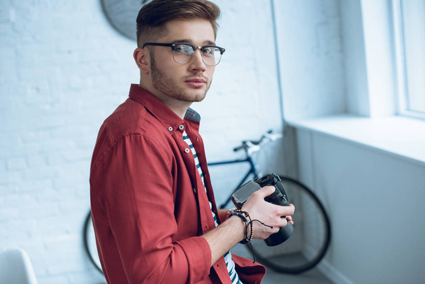 Young photographer holding digital camera in light office - Photo, Image