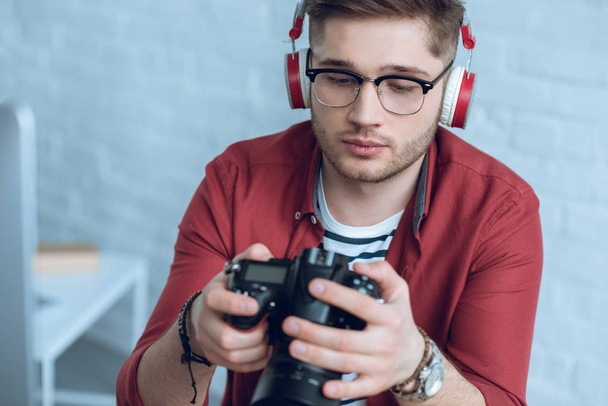 Young photographer holding digital camera in light office - Foto, Imagen