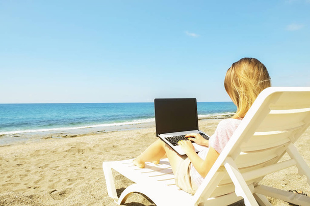 Young blonde hair woman working on laptop at the beach on sunny day. Close up of female hands typing on white notebook computer laptop, blogging, copywriting. Close up, copy space. - Photo, Image