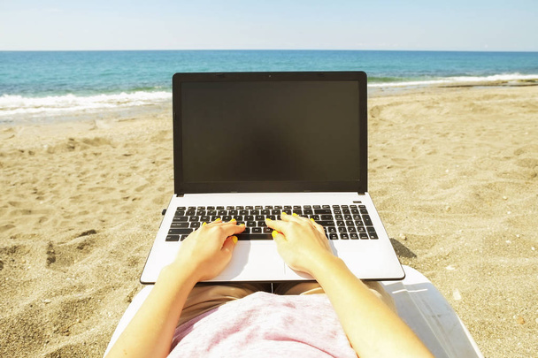 Joven mujer rubia de pelo que trabaja en el portátil en la playa en el día soleado. Primer plano de las manos femeninas escribiendo en el portátil portátil portátil blanco, blogging, copywriting. Cerrar, copiar espacio
. - Foto, Imagen
