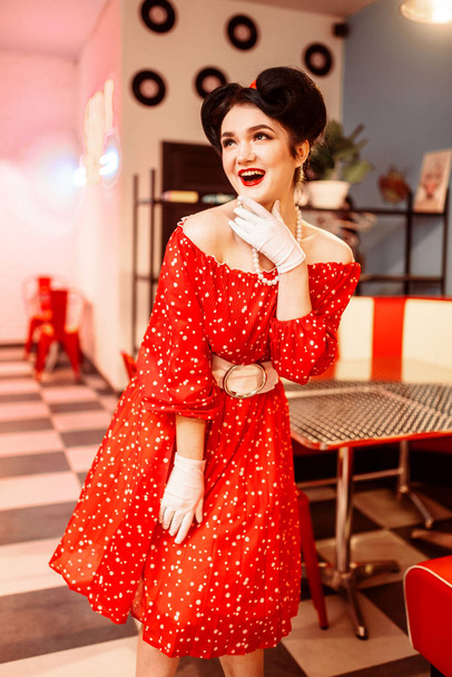 λαμπερό pin up ευτυχισμένη γυναίκα με κόκκινο φόρεμα που θέτουν στο εσωτερικό του ρετρό café  - Φωτογραφία, εικόνα