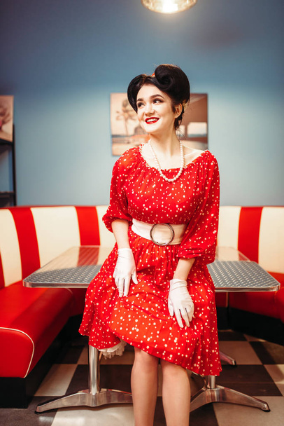 гламурная булавка счастливая женщина в красном платье позирует в интерьере ретро-кафе
  - Фото, изображение