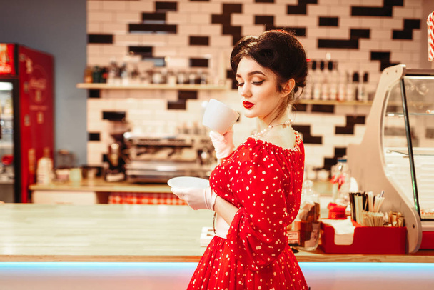 sexy pin up woman with make-up drinking coffee in retro cafe, popular retro american fashion - Zdjęcie, obraz