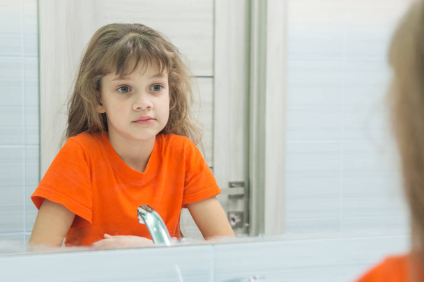 Siebenjähriges Mädchen sieht sich im Spiegel an, im Badezimmer - Foto, Bild