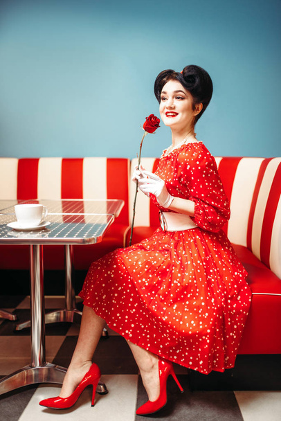 Усміхаючись підколоти жінка постановки, сидячи на дивані і Холдинг троянди, ретро американській моди  - Фото, зображення