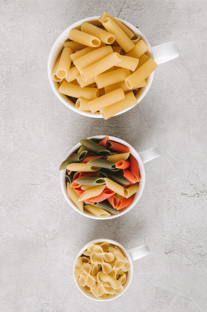 top view of various types of raw pasta in bowls standing in row on concrete tabletop - Photo, Image