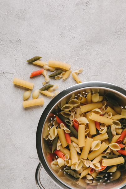 bovenaanzicht van verschillende soorten rauwe pasta in vergiet op betonnen tafelblad - Foto, afbeelding