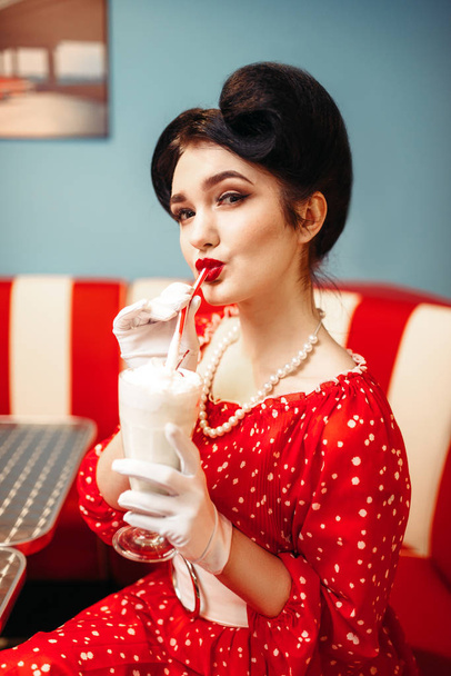 sexy pin up woman with make-up drinking milkshake in retro cafe, popular retro american fashion - Фото, изображение