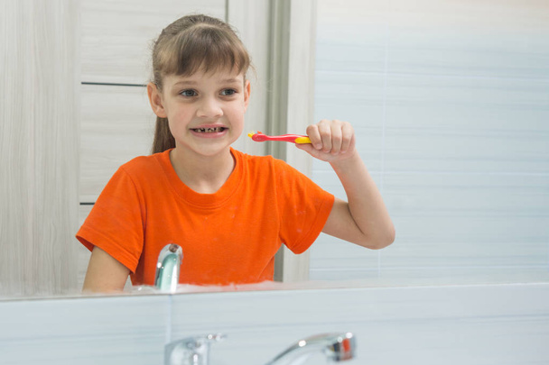 7 歳女の子が彼女の歯をブラッシングする前に鏡で自分を見てください。 - 写真・画像
