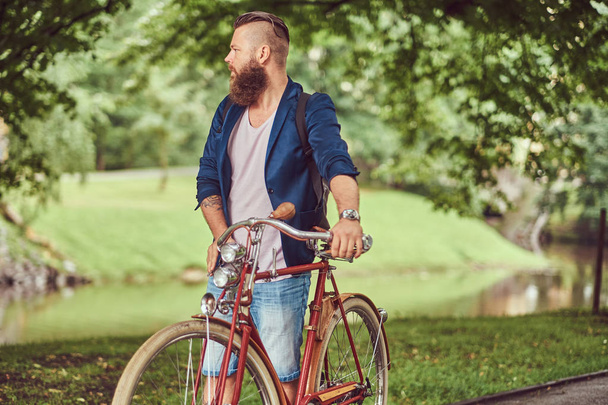 Ταξιδιώτης ντυμένοι με πρόχειρα ρούχα με ένα σακίδιο, χαλαρώνοντας σε ένα πάρκο της πόλης μετά την ιππασία σε ένα ρετρό ποδήλατο. - Φωτογραφία, εικόνα