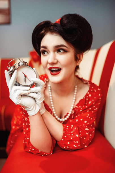 pin up mujer posando con reloj despertador, café vintage interior en el fondo
 - Foto, Imagen