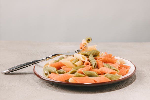 Bunte Pasta auf Teller mit Gabel auf Betonoberfläche - Foto, Bild