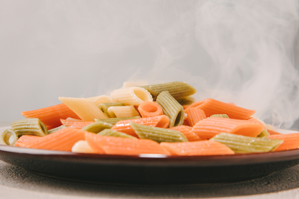 close-up shot of colorful penne pasta steaming on plate on concrete tabletop - Photo, Image