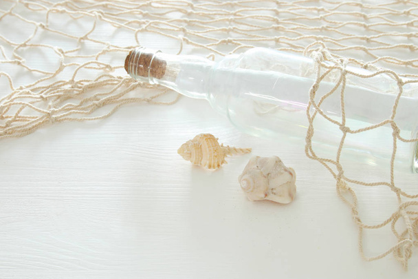 nautical concept image with letter in the bottle, seashells and fish net over white wooden table. - 写真・画像