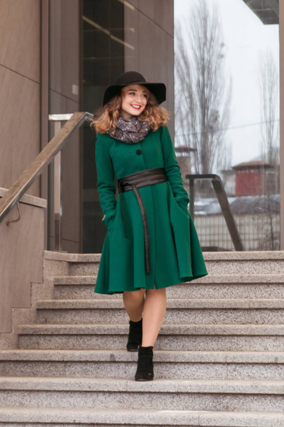 ένα κορίτσι σε ένα πράσινο παλτό και ένα μαύρο καπέλο βόλτες κάτω από τις σκάλες - Φωτογραφία, εικόνα