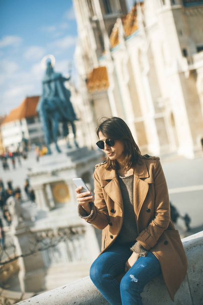 Katso trendikäs nuori nainen istuu ulkona ja käyttää matkapuhelinta
 - Valokuva, kuva
