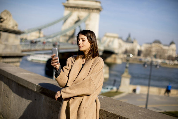 Jeune femme tenant un téléphone portable avec pont de chaîne en arrière-plan à Budapest, Hongrie
 - Photo, image