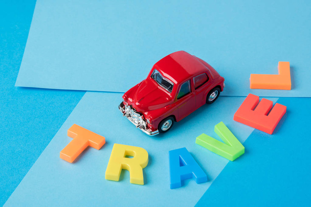 Red toy car and inscription plastic travel letters on a blue bac - 写真・画像