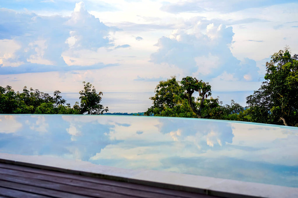 View of the beach shoreline. In the foreground, trees and sky are reflected in the pool. Island of Bali, Lovina beach. Side view with copy space - Photo, Image