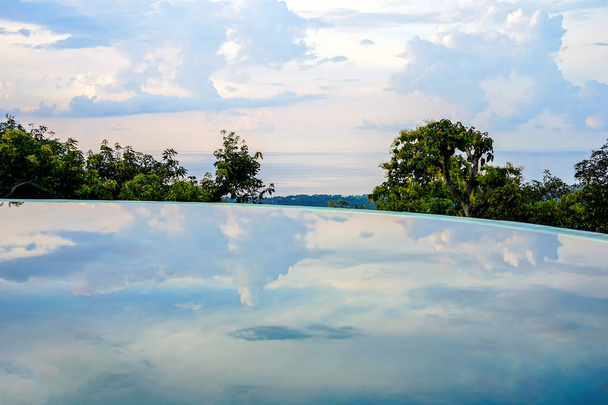 Uitzicht op de kustlijn van het strand. Op de voorgrond, worden bomen en lucht weerspiegeld in het zwembad. Eiland Bali, Lovina beach. Zijaanzicht met kopie ruimte - Foto, afbeelding