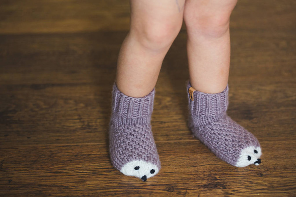 Baby voeten in de winter egel op de houten vloer sokken - Foto, afbeelding