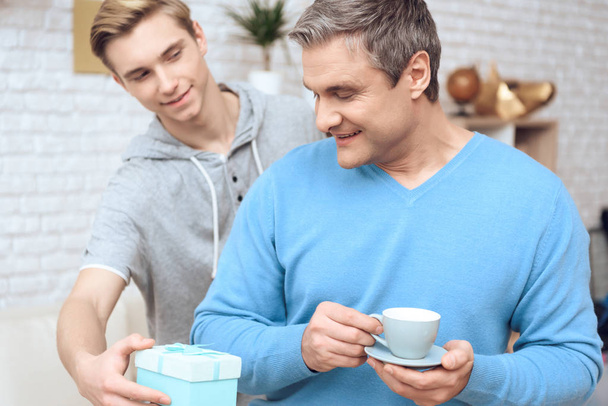 Father drinking coffee while son surprising him with birthday present - Valokuva, kuva