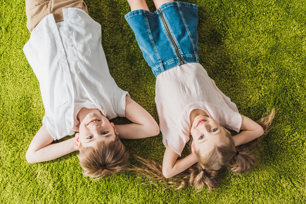 Widok z góry szczęśliwy dzieci leżąc na trawnik i uśmiecha się do kamery - Zdjęcie, obraz