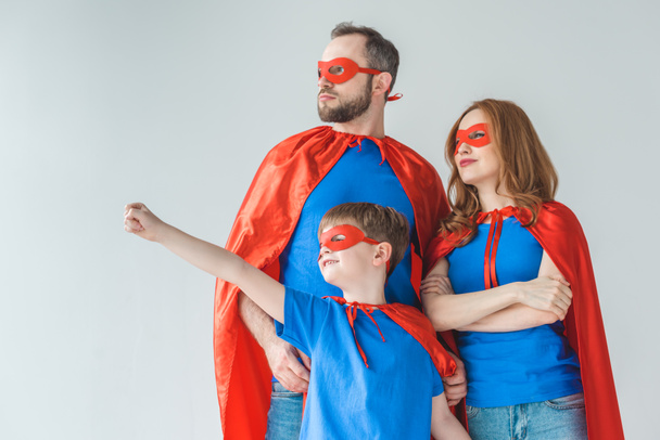 family of superheroes in masks and cloaks standing together and looking away isolated on grey - Photo, Image