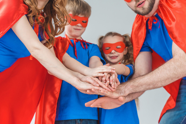 cropped shot of super family in costumes stacking hands together isolated on grey - Foto, immagini