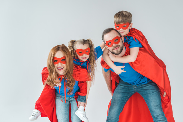 super parents piggybacking kids pretending to be superheroes isolated on grey - Foto, Imagen