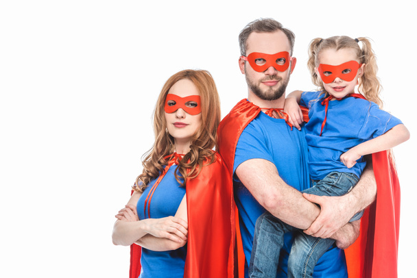 super parents with little daughter wearing masks and cloaks and looking at camera isolated on white - Photo, Image