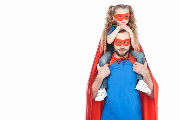 Super-Vater trägt kleine Tochter in Maske und Mantel und schaut isoliert auf weiße Kamera - Foto, Bild
