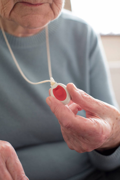 Close Up Of Unwell Senior Woman Holding Personal Alarm Button At - Foto, imagen