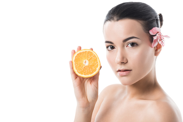 atractiva chica desnuda con la piel limpia sosteniendo naranja y mirando a la cámara aislada en blanco
 - Foto, Imagen