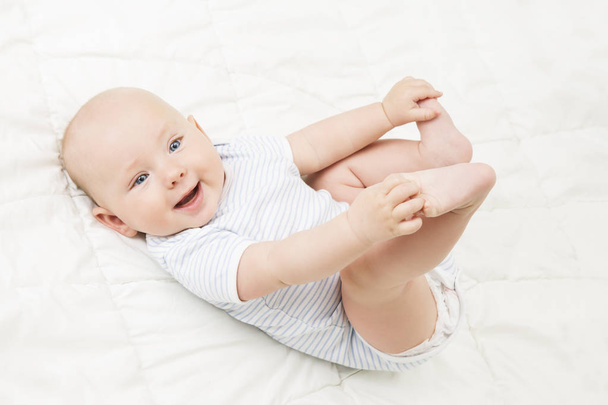 Baby Lying on Back, Happy Smiling Kid Holding Legs in Hands,  Newborn Child on White - Foto, afbeelding
