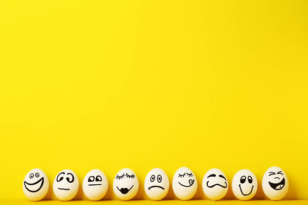 Eggs with funny faces on yellow background - Фото, изображение