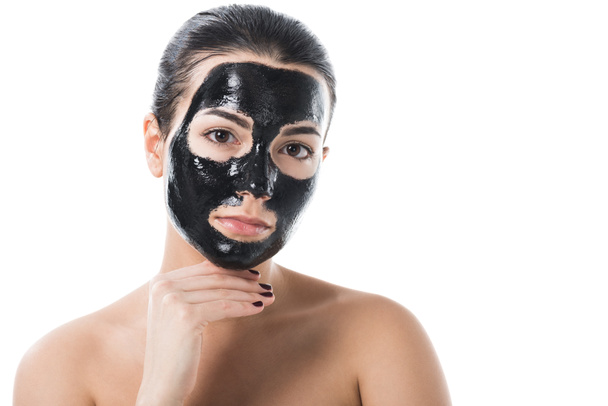 attraente ragazza in cosmetici nero argilla maschera facciale guardando la fotocamera isolata su bianco
 - Foto, immagini