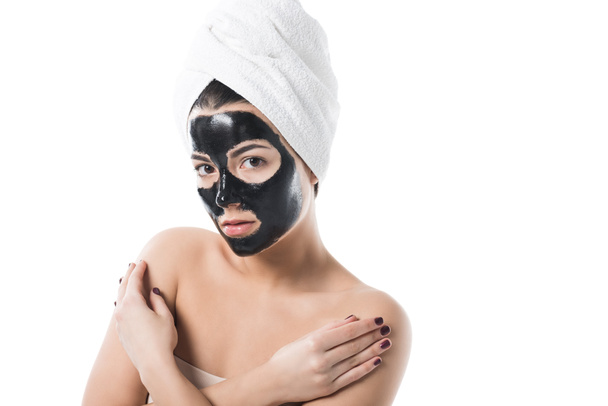 beautiful girl in cosmetic black clay facial mask and towel on head looking at camera isolated on white - Photo, Image