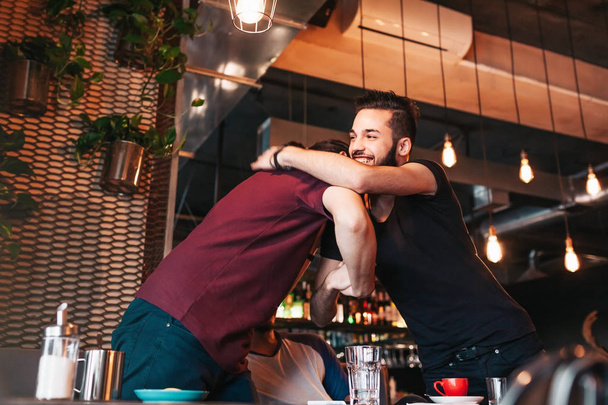 Мультирасовые мужчины встречаются со своим другом в лаундж-кафе. Настоящие эмоции лучших друзей счастливы видеть друг друга
. - Фото, изображение