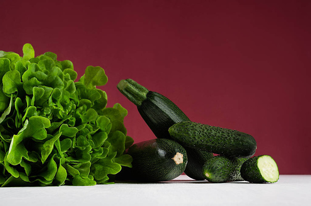 Green summer vegetables on white wood board and bordo kitchen wall. Modern elegant colorful concept kitchen interior. - Zdjęcie, obraz