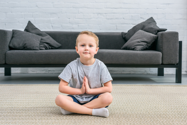 Kleiner Junge praktiziert Yoga in Lotusposition im Wohnzimmer  - Foto, Bild